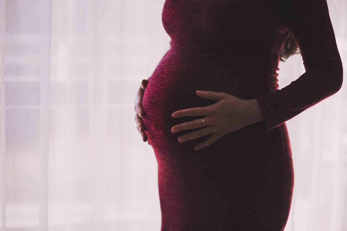 Mulher grávida com documentos na mão, sentada em corredor de escritório, com expressão preocupada