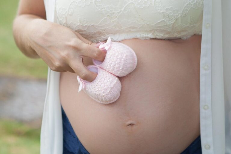 Mulher grávida sentada segurando exame de ultrassom e documentos de trabalho