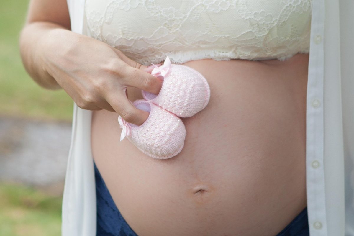 Mulher grávida sentada segurando exame de ultrassom e documentos de trabalho