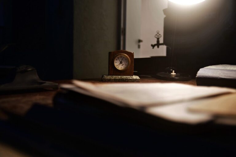 Relógio sobre a mesa de trabalho à noite, com papéis e luz acesa