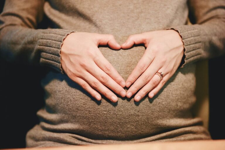 Mulher grávida com as mãos em formato de coração sobre a barriga
